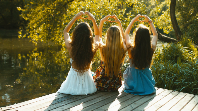 three-young-caucasian-teen-girls-sitting-on-a-wooden-pier-near-a-lake-making-heart-shapes-with-their-hands-summer-holidays-friendship-concept-blackmagic-ursa-mini-raw-graded-footage_si9zvfm4__F0000.png